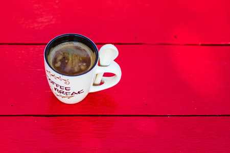 Cup of creamy homemade expresso coffee on red wooden board.
