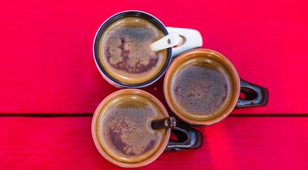 Three cups of homemade expresso coffee on red wooden board.の写真素材