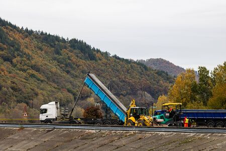 Workers waiting the heavy dump truck to unload construction materials. Construction and repair sidewalks and paving. Ramnicu Valcea, Romania, 2019.のeditorial素材
