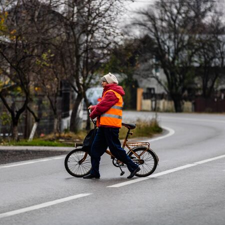 An unidentified middle aged woman riding a bicycle on a cloudy dark day. Targoviste, Romania, 2019.のeditorial素材