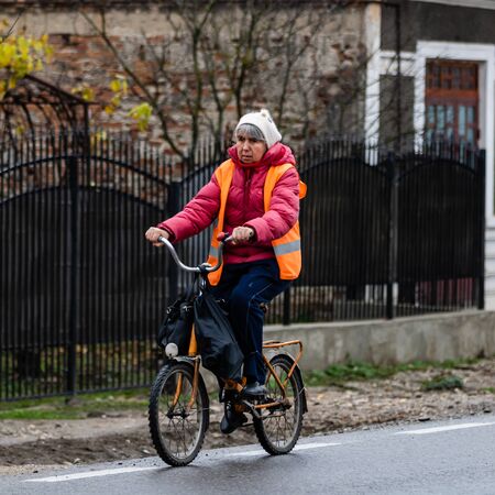 An unidentified middle aged woman riding a bicycle on a cloudy dark day. Targoviste, Romania, 2019.のeditorial素材