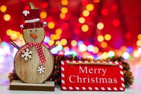 Wooden snowman figurine and Merry Christmas sign. Christmas composition on blurred lights background.の写真素材