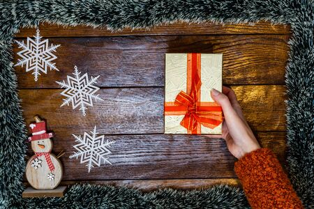 Christmas composition on wooden board with Christmas garland and decorations. Hand holding Christmas gift box.の写真素材