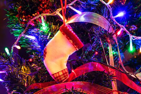 Christmas hanging decorations on fir tree. Decorated Christmas tree. Fir branch with Christmas stocking surrounded by lights and garlands.の写真素材