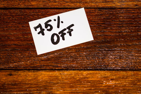 Text 75% off on white label. Label on wooden table, close up.