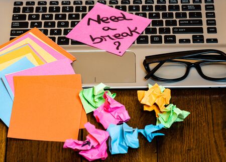 Different objects on wooden office desk. Modern wooden office desk table with laptop keyboard, pen, blank colorful sticky notes, black glasses, crumpled paperの写真素材