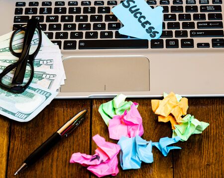 Different objects on wooden office desk. Modern wooden office desk table with laptop keyboard, pen, black glasses, money, crumpled paperの写真素材