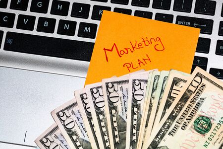 Writing on colorful sticky note Marketing plan.  Dollars money on keyboard.の写真素材