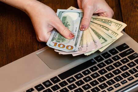 Different objects on wooden office desk. Modern wooden office desk table with laptop keyboard and hands holding dollars money.の写真素材
