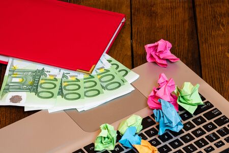 Different objects on wooden office desk. Modern wooden office desk table with laptop keyboard, money in office agenda and crumpled paper.の写真素材