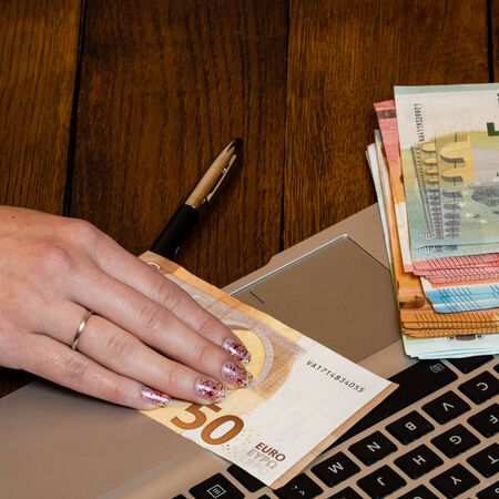 Different objects on wooden office desk. Modern wooden office desk table with laptop keyboard, pen, hand on dollars money.の写真素材