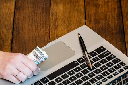 Different objects on wooden office desk. Modern wooden office desk table with laptop keyboard, pen. Business woman holding money.の写真素材