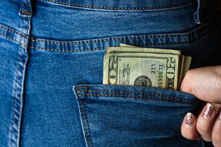 Teenage girl grabs dollar banknotes from her back pocket. Banknotes close up, money in a jeans...