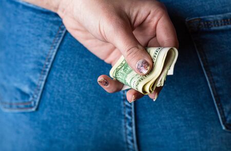 Woman hand taking money from jeans back pocket. Woman hiding money behind her back. Dollar banknotes close upの写真素材