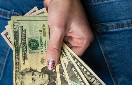 Woman hand taking money from jeans back pocket. Woman hiding money behind her back. Dollar banknotes...