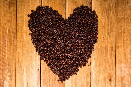 Roasted coffee beans in the form of a heart on a black wooden background, top view, copy space for text, close up coffee photoの写真素材