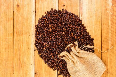 Detail of roasted coffee beans on wooden background, burlap sack, sackcloth bag with coffee beans, top view, copy space for text, close up coffee photoの写真素材