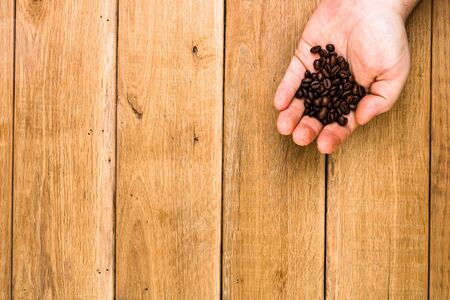 Hands holding scoop of coffee beans, healthy organic food concept on wooden background, top view, copy space for text, close up photoの写真素材