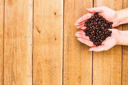 Hands holding scoop of coffee beans, healthy organic food concept on wooden background, top view, copy space for text, close up photoの写真素材