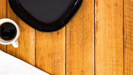 Black plate, white napkin and cup of coffee over wooden table, top view, copy space. Breakfast conceptの写真素材