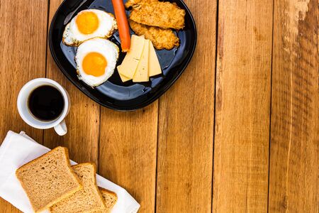 Fried egg, wholegrain toast, cheese, hotdog and cup of coffee for breakfast over wooden table, top view, copy space, breakfast conceptの写真素材