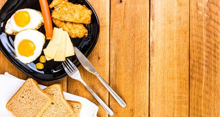 Fried egg, wholegrain toast, cheese, hotdog and cup of coffee for breakfast over wooden table, top view, copy space, breakfast conceptの写真素材