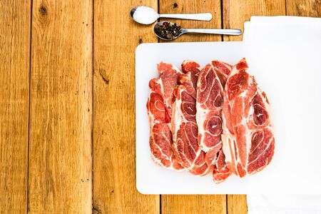 Pork chops with condiments on a white cutting board over wooden table, meat for bbq, top view, copy space, barbeque conceptの写真素材