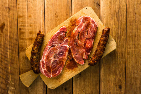 Pork chops with condiments and smoked sausage on a wooden cutting board over wooden table, meat for...