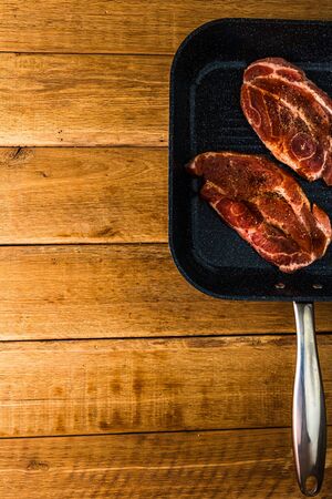Pork chops with condiments and smoked sausage on a black frying pan, over wooden table, meat for bbq, top view, copy space, barbeque conceptの写真素材