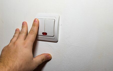 Hand turning the wall light switch on/off. Light switch close upの写真素材