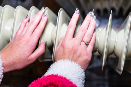 Close-up of a woman warming up her hands on a white radiator at home. Central heating conceptの写真素材