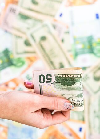 Hand giving money like bribe or tips isolated on banknotes background. EURO and USD currency banknotes close up. Reward for hard work, inflation, finance and business conceptの写真素材
