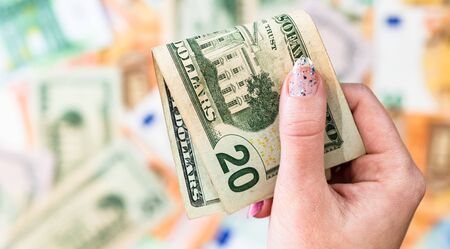Hand giving money like bribe or tips isolated on banknotes background. EURO and USD currency banknotes close up. Reward for hard work, inflation, finance and business conceptの写真素材