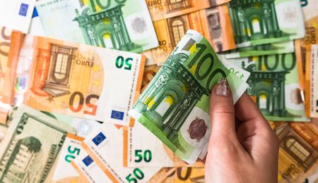 Hand giving money like bribe or tips isolated on banknotes background. EURO and USD currency banknotes close up. Reward for hard work, inflation, finance and business conceptの写真素材