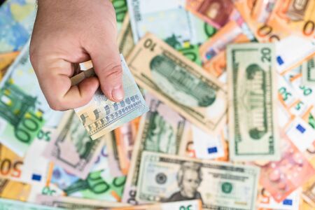 Hand giving money like bribe or tips isolated on banknotes background. EURO and USD currency banknotes close up. Reward for hard work, inflation, finance and business conceptの写真素材