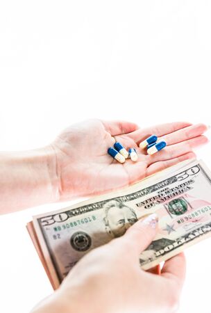 Hand holding antibiotics capsules or painkillers and money isolated on white. Medicine concept, pills close up, copy spaceの写真素材