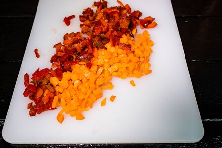 Fresh and frozen chopped vegetables,  Chopped carrots  and red bell pepper on white cutting board.の写真素材