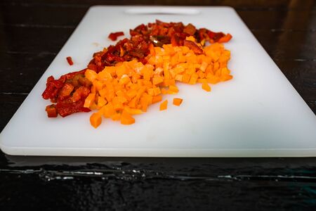 Fresh and frozen chopped vegetables,  Chopped carrots  and red bell pepper on white cutting board.の写真素材