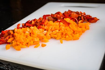 Fresh and frozen chopped vegetables,  Chopped carrots  and red bell pepper on white cutting board.の写真素材