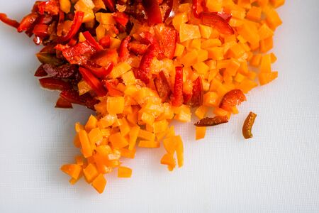 Fresh and frozen chopped vegetables,  Chopped carrots  and red bell pepper on white cutting board.の写真素材