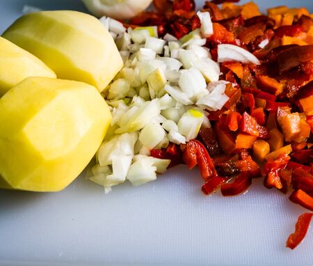 Fresh and frozen chopped vegetables,  Chopped carrots, potatoes, onions and red bell pepper on white cutting board.の写真素材