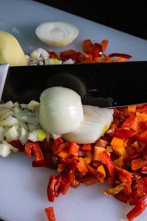 Fresh and frozen chopped vegetables,  Chopped carrots, potatoes, onions and red bell pepper on white cutting board.の写真素材