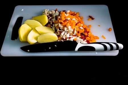 Fresh and frozen chopped vegetables,  Chopped carrots, potatoes, onions and red bell pepper on white cutting board.の写真素材