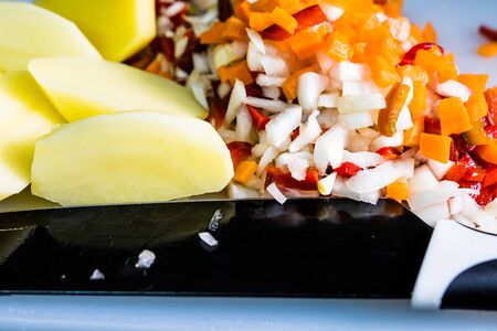Fresh and frozen chopped vegetables,  Chopped carrots, potatoes, onions and red bell pepper on white cutting board.の写真素材