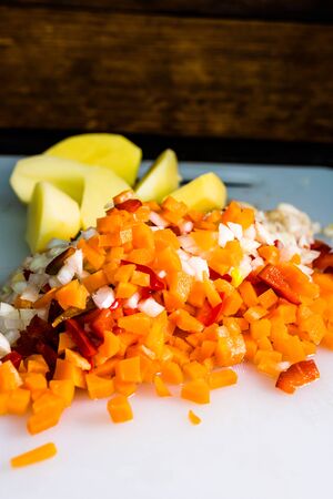 Fresh and frozen chopped vegetables,  Chopped carrots, potatoes, onions and red bell pepper on white cutting board.の写真素材