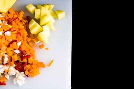 Fresh and frozen chopped vegetables,  Chopped carrots, potatoes, onions and red bell pepper on white cutting board.の写真素材