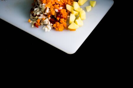 Fresh and frozen chopped vegetables,  Chopped carrots, potatoes, onions and red bell pepper on white cutting board.の写真素材