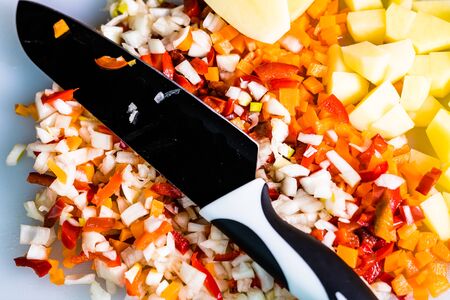 Fresh and frozen chopped vegetables,  Chopped carrots, potatoes, onions and red bell pepper on white cutting board.の写真素材