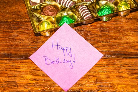 Happy birthday text on memo post reminder, near a golden box with chocolate pralines.の写真素材