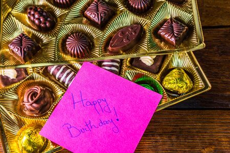 Happy birthday text on memo post reminder, near a golden box with chocolate pralines.の写真素材